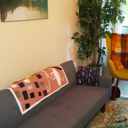 Image of a grey couch with a hand-stitched quilt folded over and lying across the back of the it.